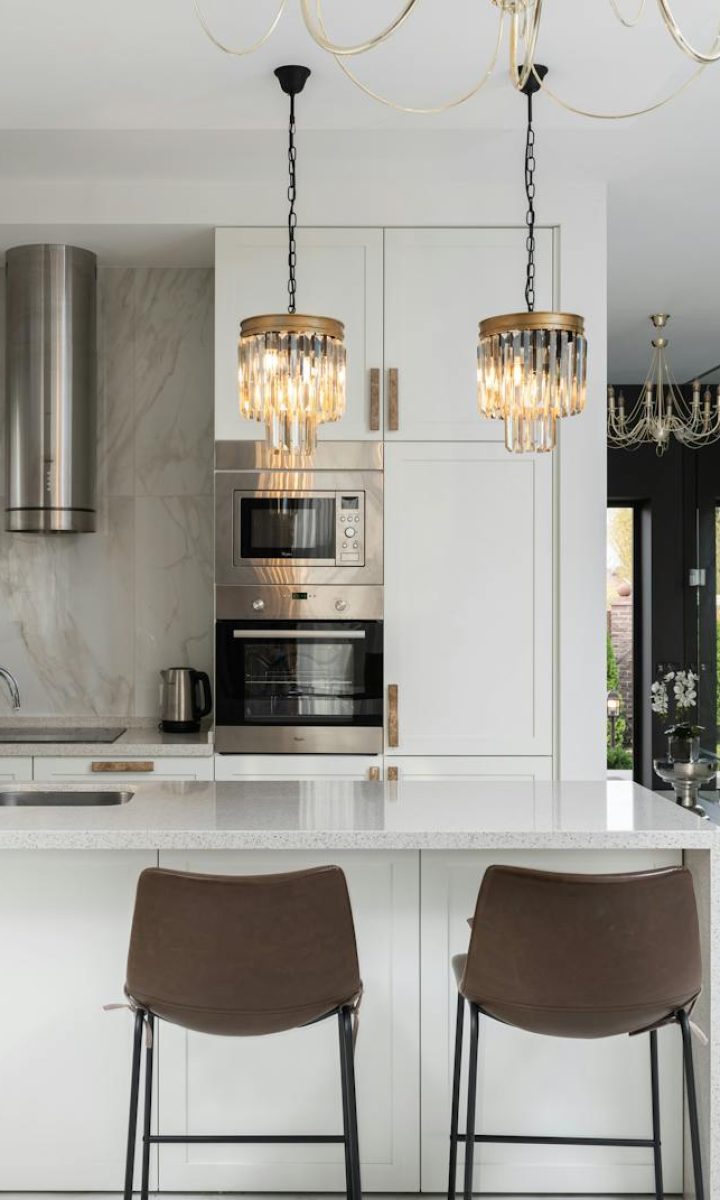 Photo by Max Vakhtbovycn Interior of contemporary kitchen with modern appliances and chairs at white counter near wall with shelves in spacious apartment near stairs