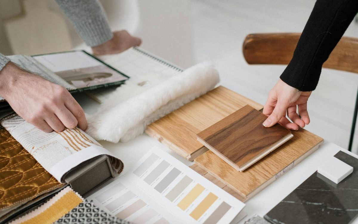 Hands selecting and comparing textile and wood samples for interior design.