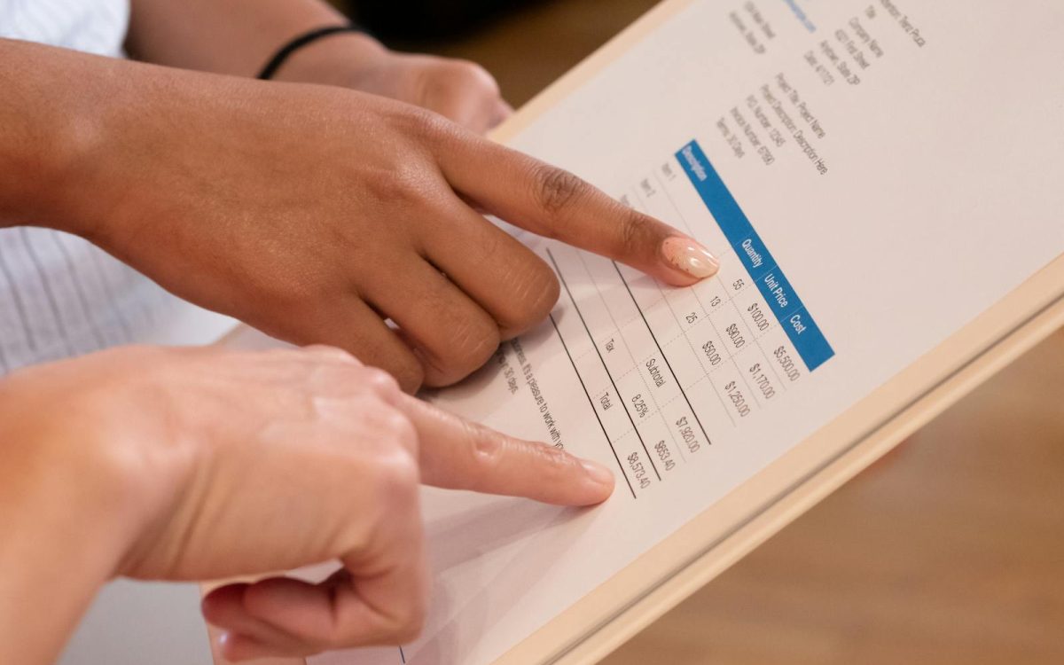 Two people pointing at financial details on a document, highlighting invoice analysis.