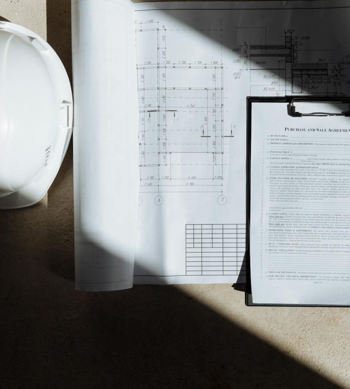 Top view of construction documents and hard hat in sunlight, capturing planning essence.
