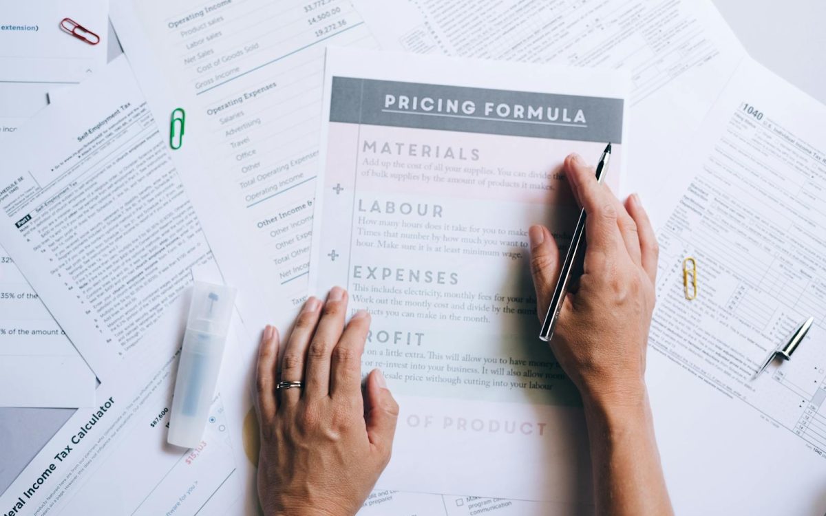 Hands organizing business documents and pricing formula papers on an office desk.